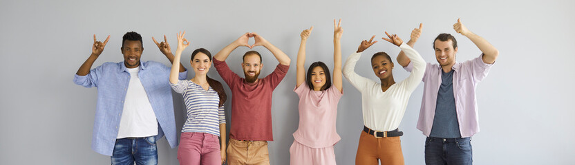 Casual header portrait happy diverse multiracial multiethnic people standing on grey studio background show different non verbal body language hand gestures like OK, thumbs up or rock n roll horn sign © Studio Romantic
