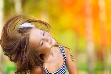 Naklejka premium Portrait of Little caucasian girl wind with flying hair, against green of summer park.