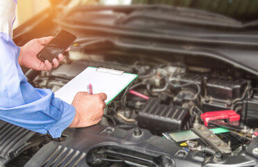 Fototapeta premium Hand mechanic hold check sheet paper and smart phone for basic checking a engine of car,maintenance and service check in garage
