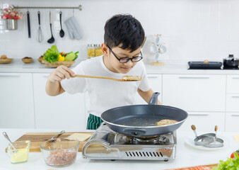 Asian boy in glasses enjoying smell of freshly fried patty while cooking burgers in modern kitchen...