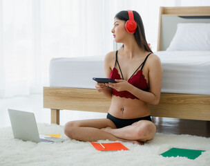 Beautiful young naughty sexy girl on red bra sit back against white bed end while studying lecture...
