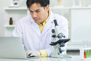 Close up face. Asian man smiling scientist looking in computer laptop microscope while working on medical research in science laboratory. Concept research virus coronavirus covid19.
