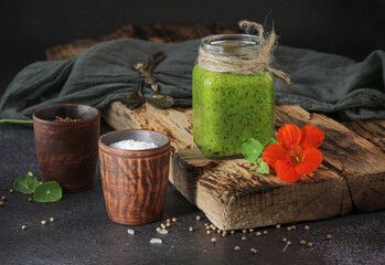 Spicy green nasturtium sauce in a glass jar on a wooden vintage stand a fresh nasturtium flower.