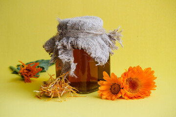 Medicinal tincture of calendula in glass jar on a yellow background.