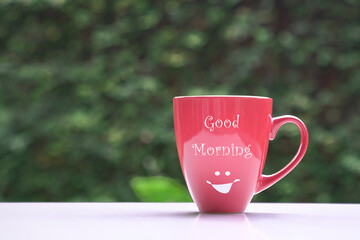 Good morning message on red coffee cup, on green nature background. Copy space.