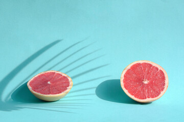 Summer still life with two cut grapefruits with palm leaves harsh shadows. On blue background.