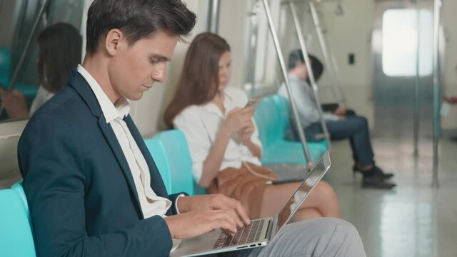 Young Caucasian white businessman sitting using laptop computer working on the subway train in the morning during going to work, people transportation concept