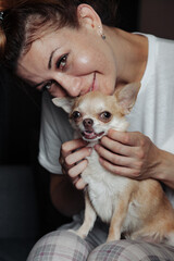 Pretty mature woman with Chihuahua dog on dark sofa