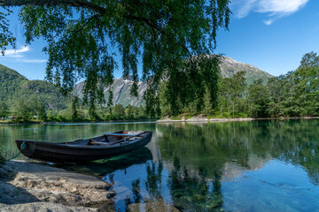 Boat under a tree in a green river with view to the mountains. 