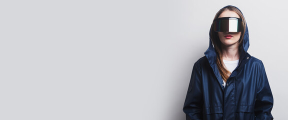 Young woman of the future in virtual reality glasses, in a blue jacket on a light background. Banner
