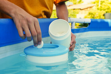 Hand holding white chlorine tablets over swimming pool skimmer. Chlorination of water in pool for...