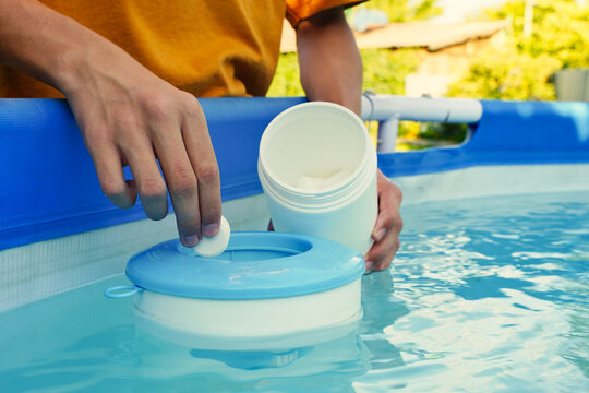Hand holding white chlorine tablets over swimming pool skimmer. Chlorination of water in pool for disinfection and prevention against the development of microbes.