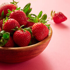 Strawberries in a wooden bowl on a pink background