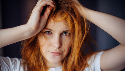 Fototapeta premium Portrait of beautiful adult young woman with red tousled hair, close-up, blurred background. Sexy brunette touches her long hair and looks at camera.