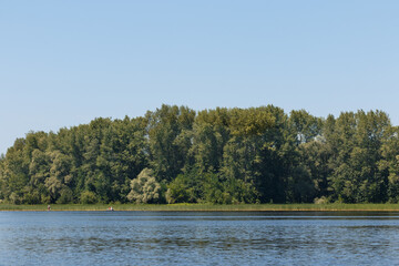 summer landscape with a river, floating people on boats in the distance, green beach, smooth water