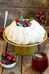 Pavlova cake with blueberry curd, cherries, blueberries and sage. Side view. Wooden background.