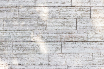 The texture of a gray stone wall made of rectangular marble blocks. Sunlight on the masonry.