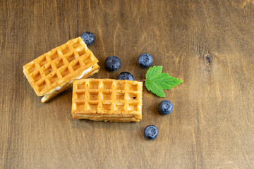 Soft Belgian waffles with blueberries on the background of a brown wooden table with a natural pattern, a copy of the space. Rustic style