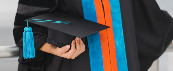 Close-up shot of a university graduate in graduation gown holding a degree certification with...