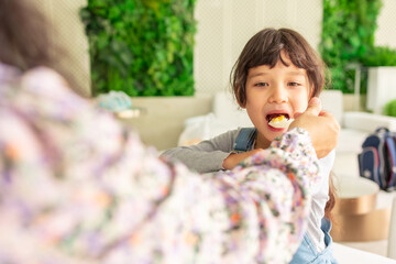 Mixed race  beautiful girl having breakfast before go to school.Mother and daughter having healthy breakfast on table in room.