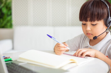 Naklejka na ściany i meble Asian boy sit at desk study online on laptop, smart little kid handwrite in notebook learning using internet lessons on quarantine, homeschooling concept.