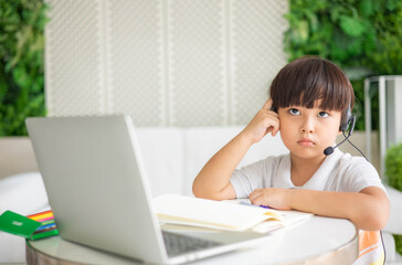 Asian boy sit at desk study online on laptop, smart little kid handwrite in notebook learning using internet lessons on quarantine, homeschooling concept.