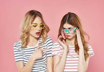 two girlfriends stand side by side in striped t-shirts glasses fashion summer pink background