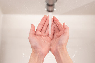 Fototapeta premium Washing hands for coronavirus outbreak prevention: closeup of unrecognizable caucasian female holding palms under clean water flow from faucet in bathroom sink. Cleanliness, hygiene and health concept