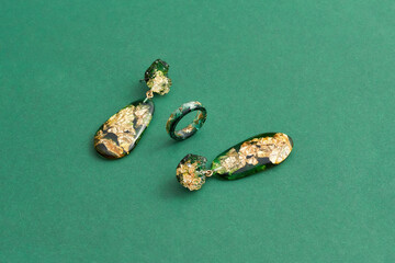 Set of a ring and dangle earrings made of epoxy resin with golden foil inside isolated over green...