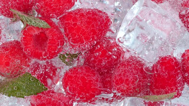 Super Slow Motion Shot of Fizzing Water with Raspberries and Ice Cubes in Glass at 1000 fps.
