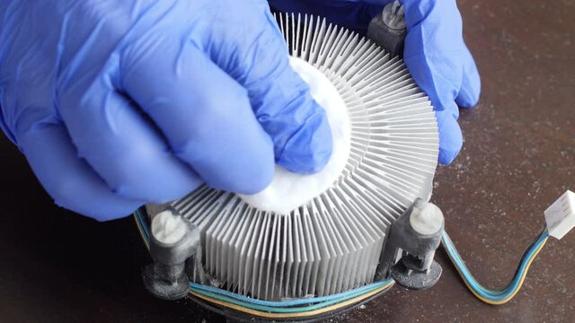 Electronics repair technician carefully cleans the aluminum heatsink for a computer processor on the motherboard of a desktop computer of old coolant with a cotton pad and cleaning fluid. Close up