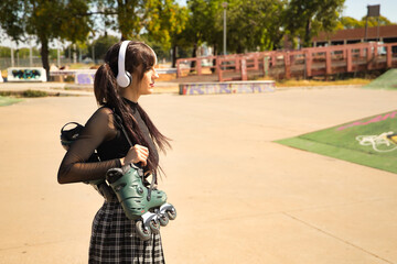 Young and pretty girl with pigtails, punk style, white headphones and inline skates hanging from...