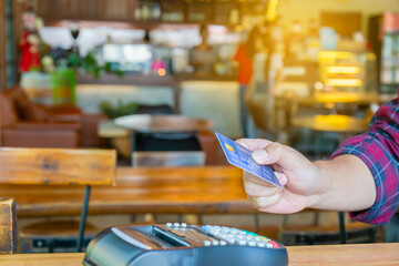 Man holding credit card with a credit card reader machine at bar counter, Hand of customer paying with contactless credit card with NFC technology.