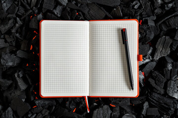An open checkered notebook lying on a dark charcoal with red flashes of heat.