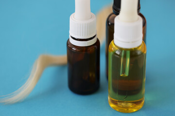Many jars of cosmetic oil standing near lock of white hair on blue background closeu
