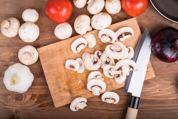 Ingredients for cooking vegetarian stew - chopped mushrooms on a cutting board with a knife,...