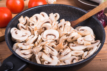 Vegetarian stew ingredients - chopped mushrooms in a skillet, tomatoes and onions on the table