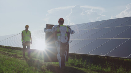 Male technician in exoskeleton carrying solar panel to coworker