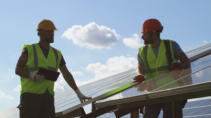 Male engineers examining photovoltaic panels on sunny day