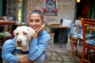 A young beautiful girl is posing for a photo in the bar in a hug with her dog. Leisure, bar,...