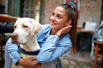 A young beautiful girl in a hug with her dog while they spending a time in the bar together....