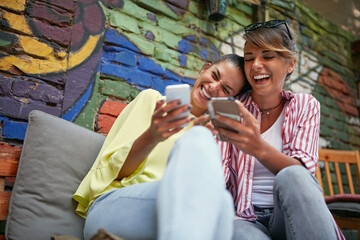 two gorgeous caucasian females laughing loud looking something on their cell phones