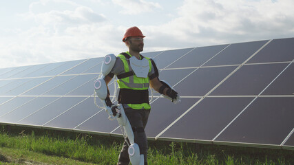 Male engineer in exoskeleton walking on solar plant - obrazy, fototapety, plakaty