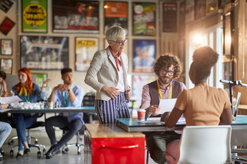 Elderly female boss is checking employees work in the office