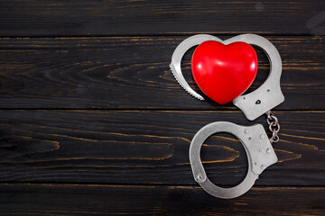 red heart and handcuffs on a wooden background