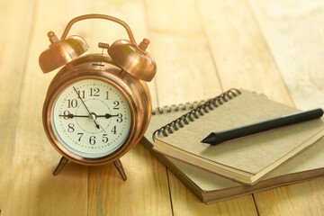 Golden alarm clock with note book on wooden table and golden light in the morning.