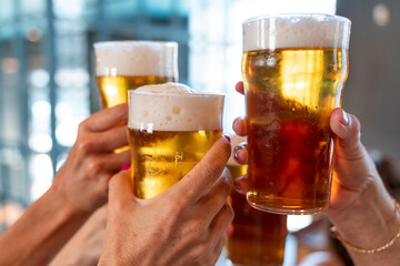 group of women toasting with glasses of beer in a pub. Close-up on the hands