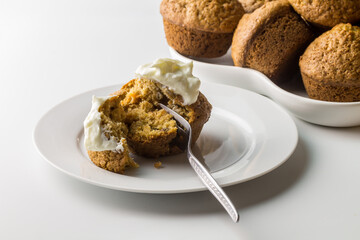 Carrot cinnamon cake muffin with yogurt on white serving plate with muffins in background isolated...