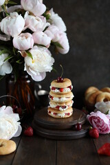 Custard rings with curd cream and berries on a dark table with a bouquet of peonies. Still life with flowers and sweets.
