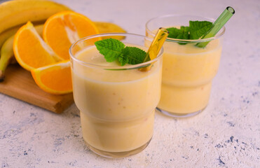 Two glasses of orange banana smoothie with a mint leaf on a white background.